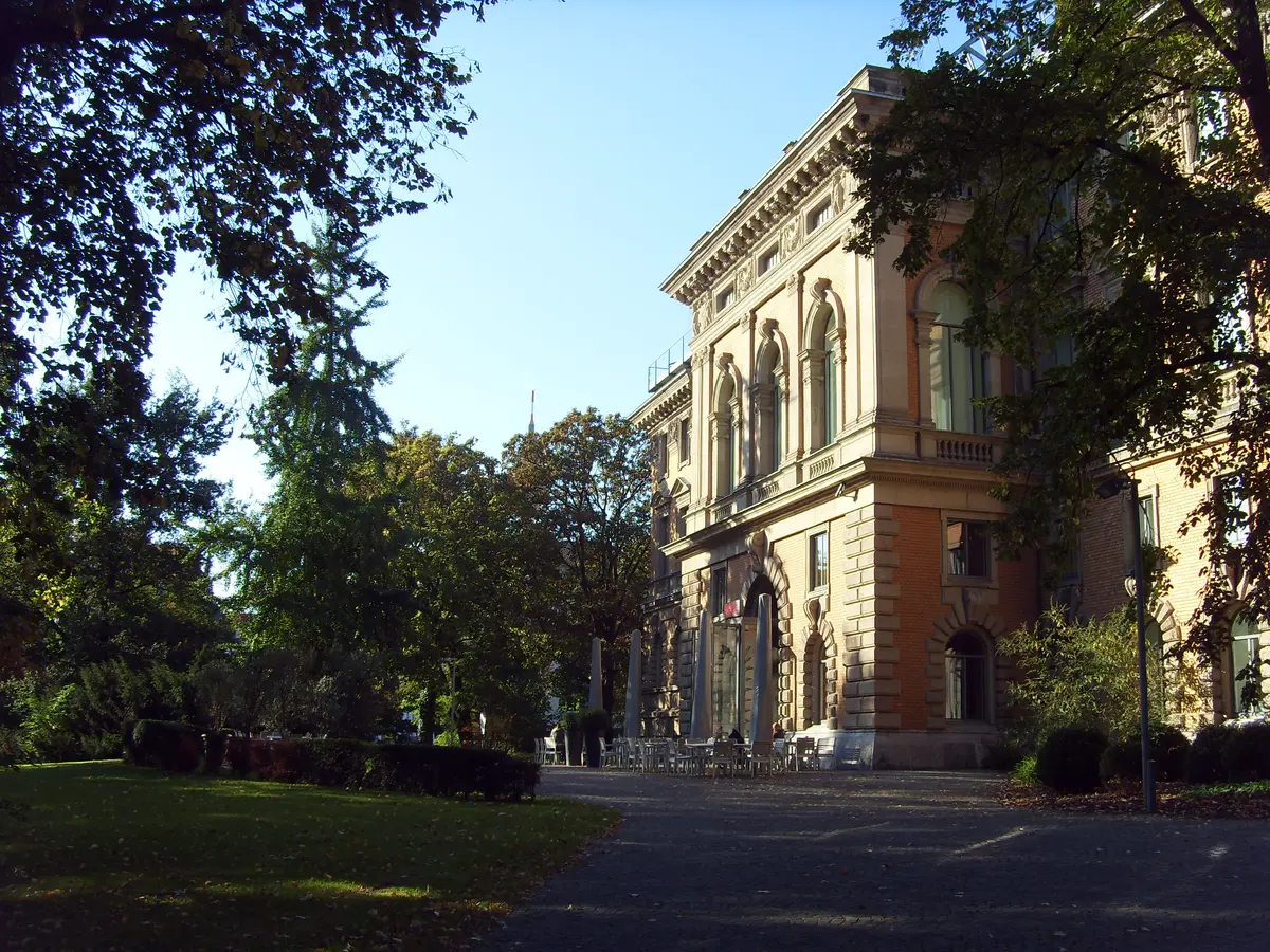 Außenansicht des Kunstpalasts Düsseldorf am Ehrenhof mit roten Säulen und Bäumen