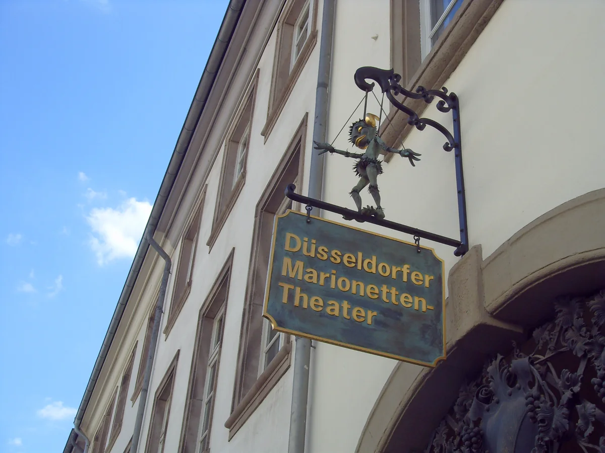 Schild des Düsseldorfer Marionetten-Theaters an einer historischen Fassade mit bronzener Marionettenfigur